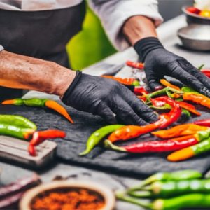The chef handles the vibrant array of spicy chili peppers with black gloves, ensuring safety